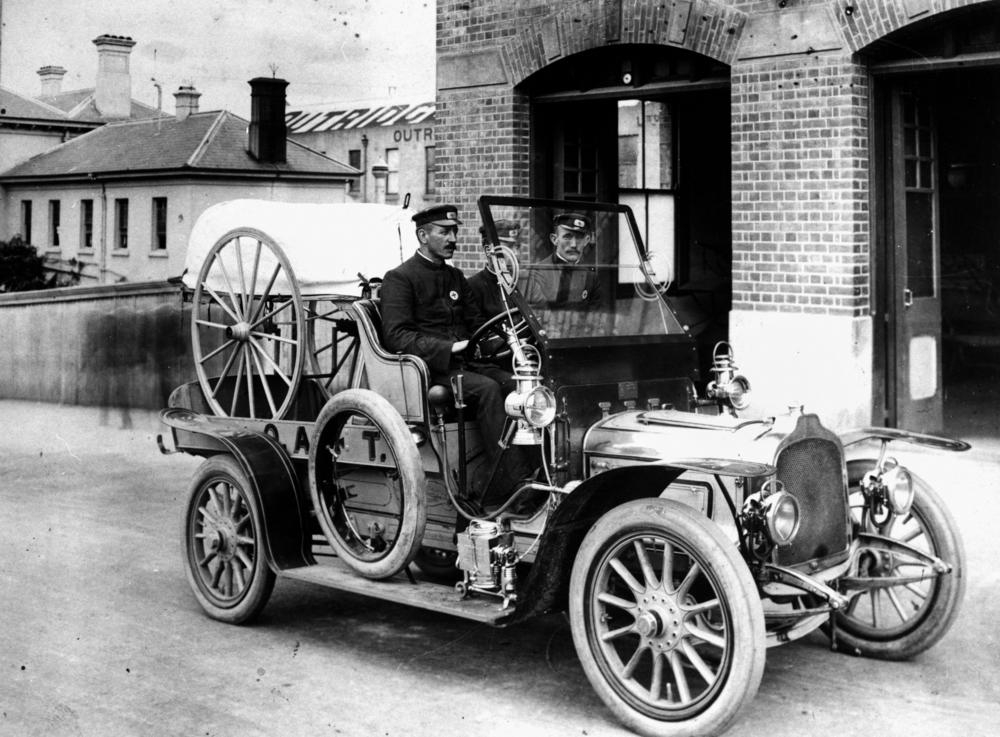 Drei Männer in Uniform sitzen auf dem Vordersitz eines offenen, historischen Automobils.